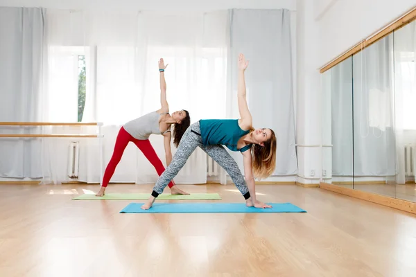 Две женщины, занимающиеся растянутой позой треугольника, utthita trikonasana yoga asana — стоковое фото