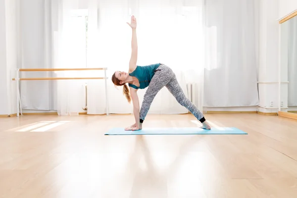 Молодая гибкая блондинка практикующая треугольную позу в центре йоги — стоковое фото