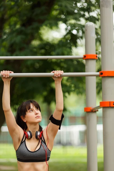 Fit woman with headphones preparing to do pull ups — Stock Photo, Image