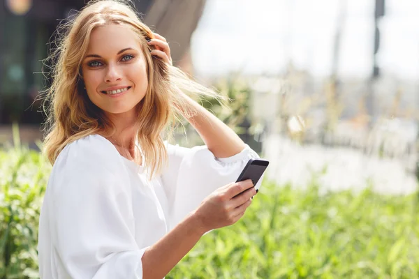 Mujer caucásica sonriente suave con teléfono celular descansando en el parque verde — Foto de Stock