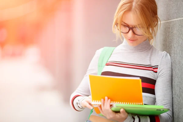 girl looks in book outside wall of building