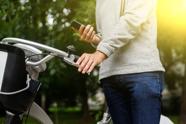 Człowiek w sweter i dżinsy z telefonu obok roweru — Zdjęcie stockowe