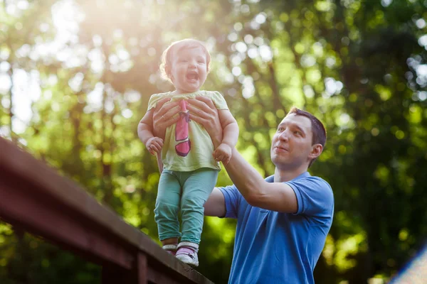 Far stöder lilla dotter står på bron i park — Stockfoto