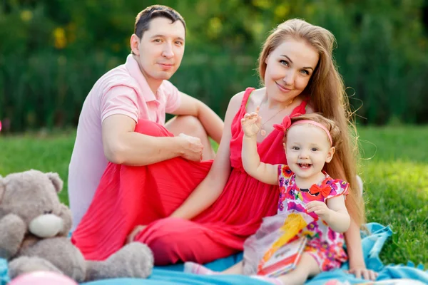 Jeunes parents avec fille et livre assis sur plaid — Photo