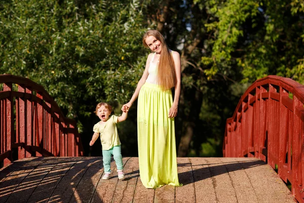 Mom and little daughter by hand go on wooden bridge — Stock Photo, Image