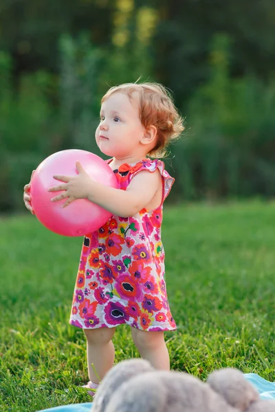 Kleines Mädchen hält rosa Ball auf Rasen im Park — Stockfoto