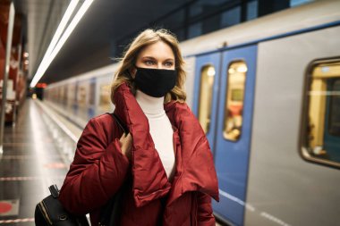 Metroda maskeli ve kırmızı ceketli bir kadın var.