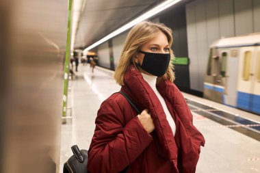 Metroda maskeli ve kırmızı ceketli bir kadın var.