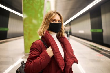 Metroda maskeli ve kırmızı ceketli bir kadın var.