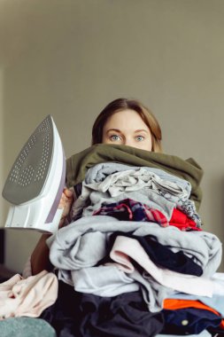 Büyük bir elbise yığınının arkasında ütülü bir kız. ütü yapmadan önce