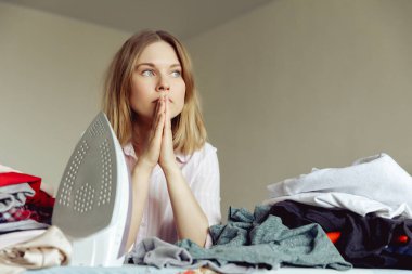 Üzüntülü genç kadın evde giysileri ütülüyor