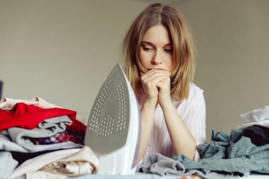 Üzüntülü genç kadın evde giysileri ütülüyor