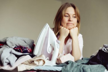 Üzüntülü genç kadın evde giysileri ütülüyor