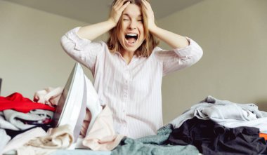 kızgın genç kız evde giysileri ütülüyor.