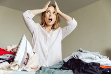 kızgın genç kız evde giysileri ütülüyor.