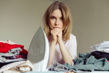 Üzüntülü genç kadın evde giysileri ütülüyor