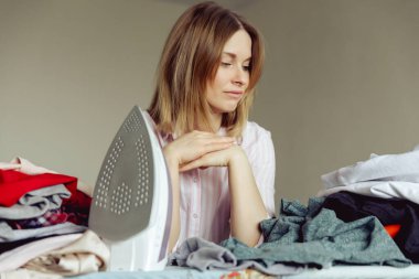 Üzüntülü genç kadın evde giysileri ütülüyor