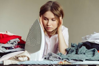 Üzüntülü genç kadın evde giysileri ütülüyor