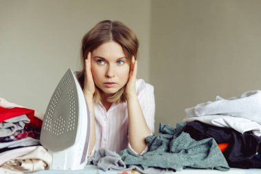 Üzüntülü genç kadın evde giysileri ütülüyor