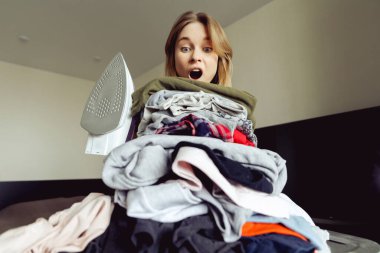 Büyük bir elbise yığınının arkasında ütülü bir kız. ütü yapmadan önce