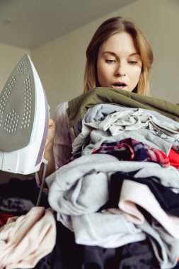 Büyük bir elbise yığınının arkasında ütülü bir kız. ütü yapmadan önce