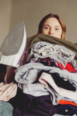Büyük bir elbise yığınının arkasında ütülü bir kız. ütü yapmadan önce