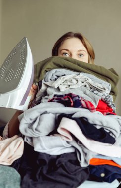 Büyük bir elbise yığınının arkasında ütülü bir kız. ütü yapmadan önce