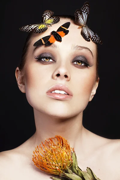Portrait of beautiful young woman with butterflies and exotic flower on black background — Stock Photo, Image