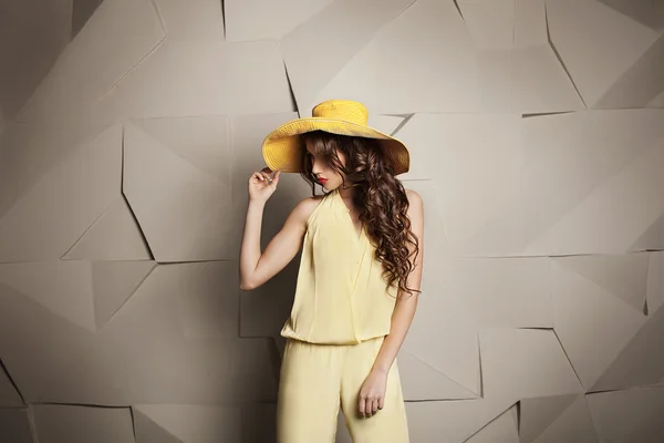 Sarı şapka ve gri grafik arka plan tulum kıvırcık saç modeli olan kadın.