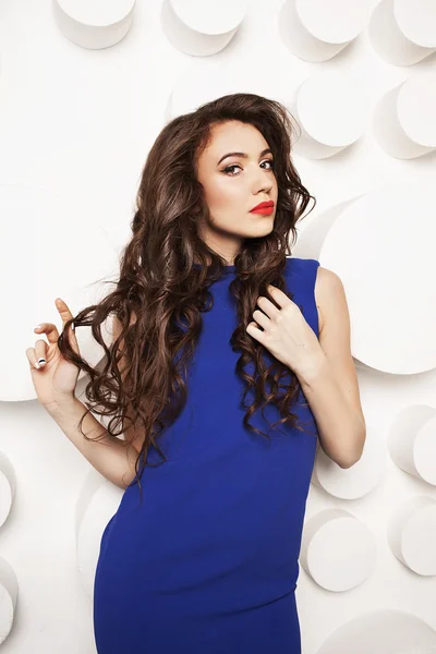 Portrait of beautiful young woman with curly long brown hair in blue dress