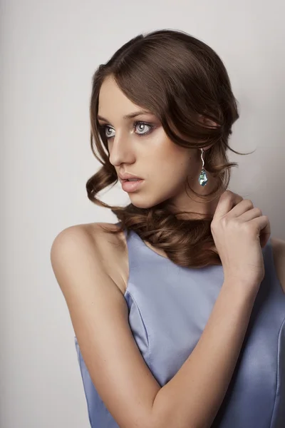 Schöne junge Frau in blauem Kleid und Ohrringen. lizenzfreie Stockbilder