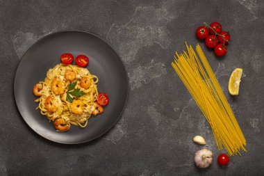 Gri taşlı arka planda malzemeli karidesli spagetti. Spagetti, domates, sarımsak, limon. Yukarıdan görüntüle.