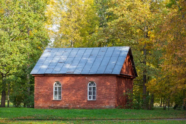 An old small one-storey house made of red brick against a background of lawn and trees. — Stock Photo, Image