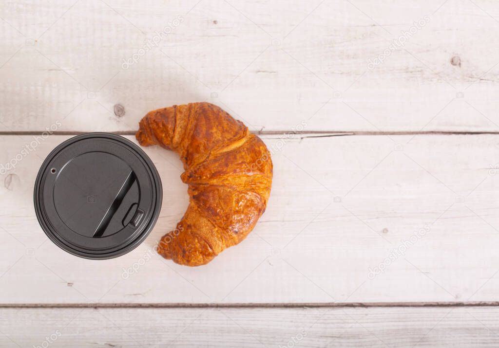 Paper cup of coffee and croissant on a light wooden background. Close-up. copy space. Free space for text. top view.