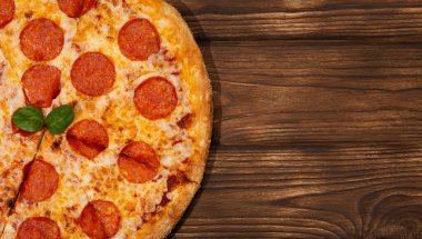 Lezzetli taze biberli pizza ve ahşap arka planda domates fesleğeni. Pepperonili pizzanın en iyi manzarası. Düz yatıyordu. Metin için kopyalama alanı ile. Pankart