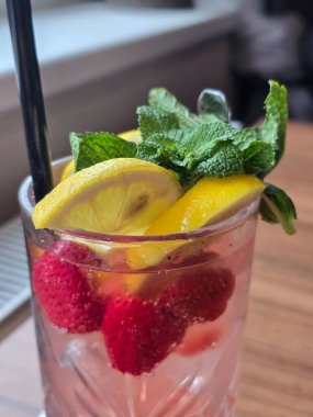 Tahta bir masada buzlu ve naneli bir bardak kırmızı meyve suyu.