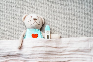 Termometresi olan oyuncak ayı bebek battaniyesiyle kaplı. Fotokopi alanı olan çocuk sağlığı konsepti fotoğrafı.