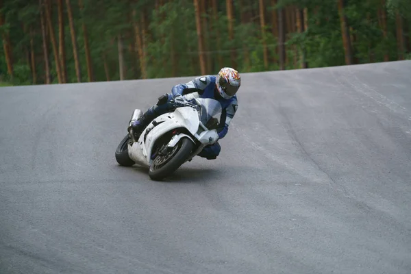 アスファルトの道路でバイクに乗る男 オートバイで青いスーツで白いスポーツバイク — ストック写真