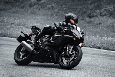 man riding motorcycle in asphalt road. Motorcyclist in black suit at black sport motorcycle.