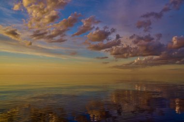 Denizin üzerinde güzel bir gün batımı, suda yansıması, gökyüzünde görkemli bulutlar.