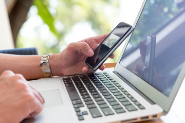 Smartphone ile dizüstü bilgisayar kullanan adam