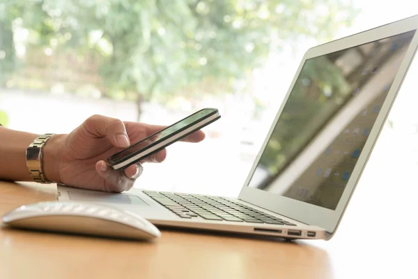 Mano hombre utilizar el teléfono inteligente con el ordenador portátil —  Fotos de Stock