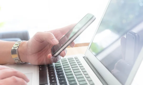 Dizüstü bilgisayar, pencere ışık ile görüntü sahne ile akıllı telefon kullanan adam — Stok fotoğraf