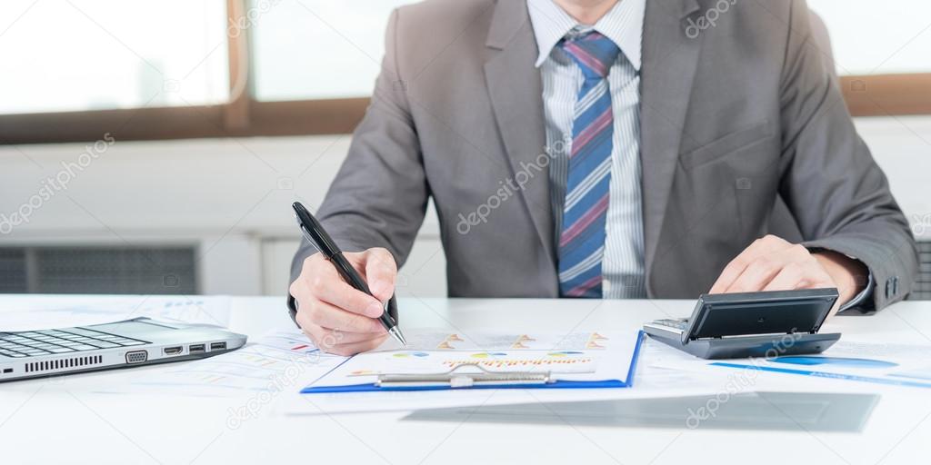 Businessman analyzing report on chart with laptop and calculator