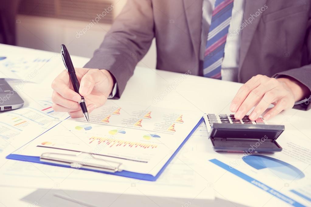 Businessman analyzing report on chart with laptop and calculator