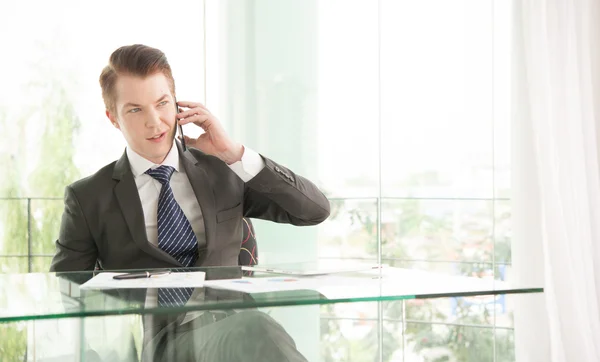 Красивый бизнесмен в костюме говорит по телефону в офисе — стоковое фото