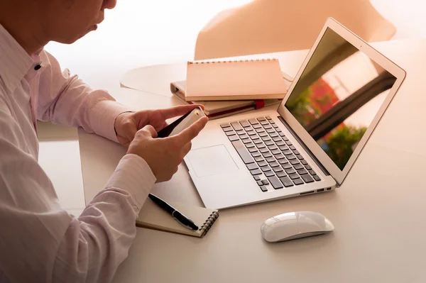 Hombre usando el teléfono inteligente con el ordenador portátil en el escritorio — Foto de Stock