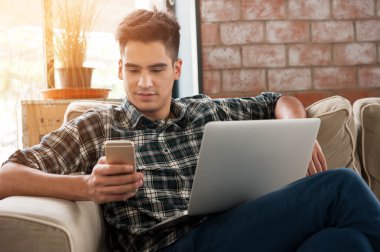 İş adamı, kafedeki kanepede akıllı telefon ve dizüstü bilgisayar kullanıyor.