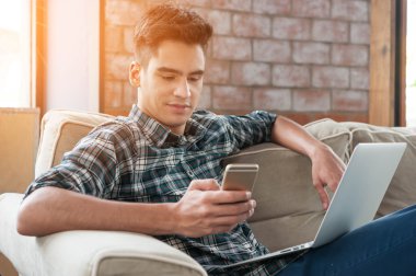 Smartphone ve kahve kanepe üzerinde yazma dizüstü kullanarak iş adamı