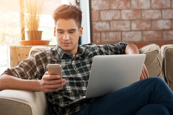 Бізнесмен використовує смартфон і ноутбук, пишучи на дивані в кав'ярні — стокове фото
